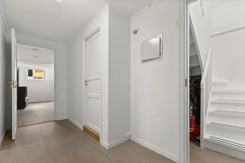 Bright and modern white hallway with stairs and open doors, showcasing minimalist interior design.