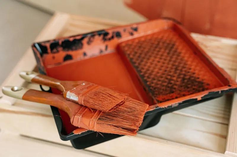 Paintbrushes resting on an orange paint tray during a painting project, indoors.