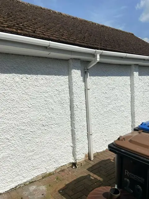 Long pebbledash wall repainted bright white beneath white guttering and a tiled roof