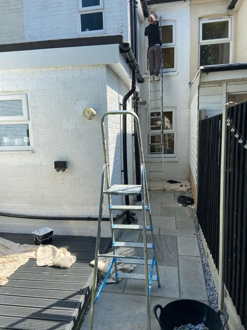 Narrow side return with white-painted brickwork, decorator on a ladder at the upper windows
