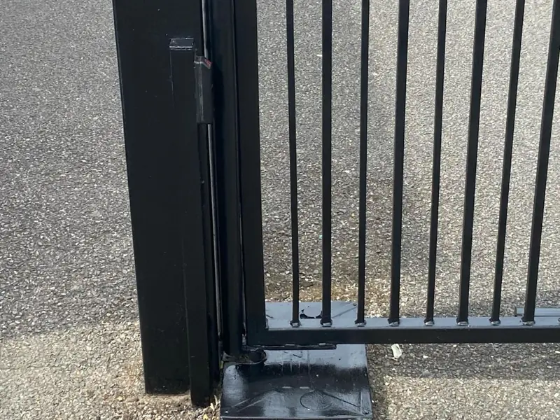 Close-up of a black gloss finish on a gate post, hinge and base plate