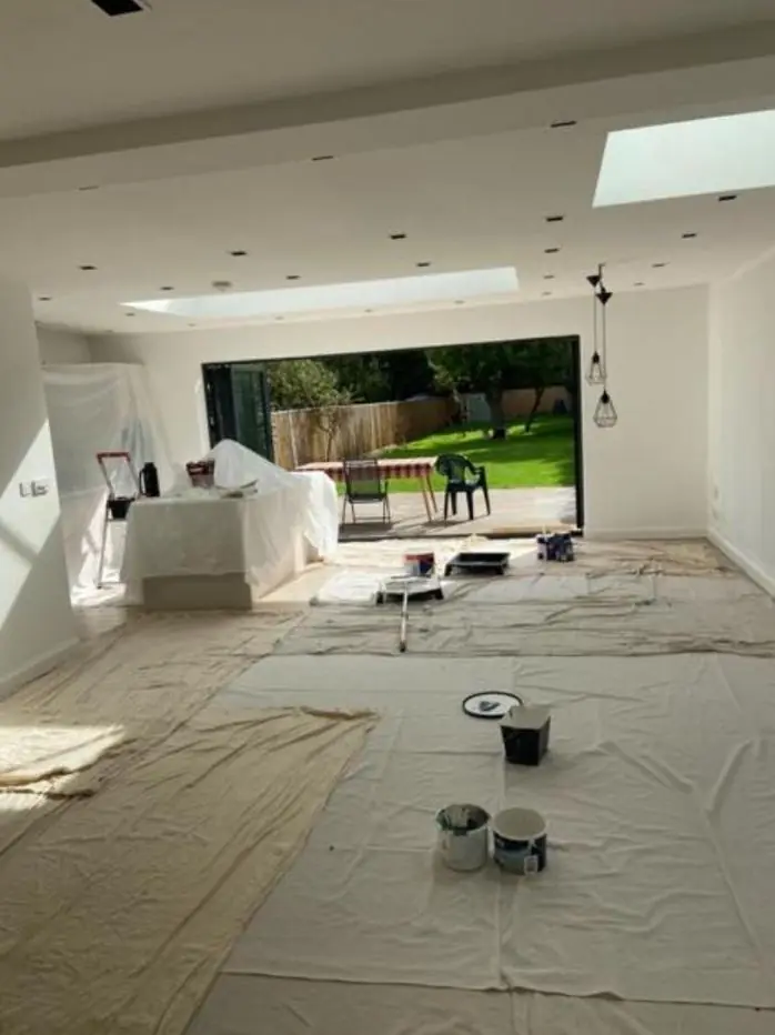 Wide view of a white-painted extension with pendant lights and paint tins on dust sheets