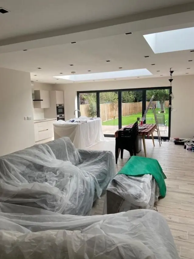 Extension walls painted pale grey with roof lanterns overhead, furniture still under sheeting