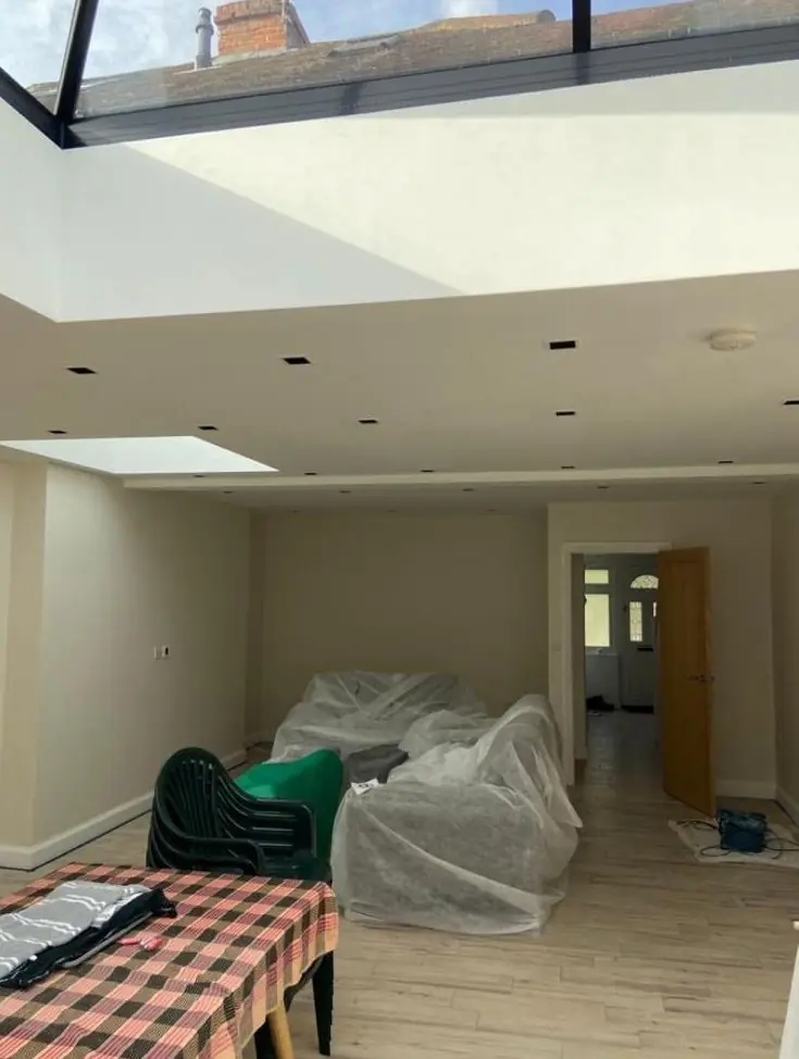 Roof lantern reveals painted white above a grey extension, sofas sheeted for protection